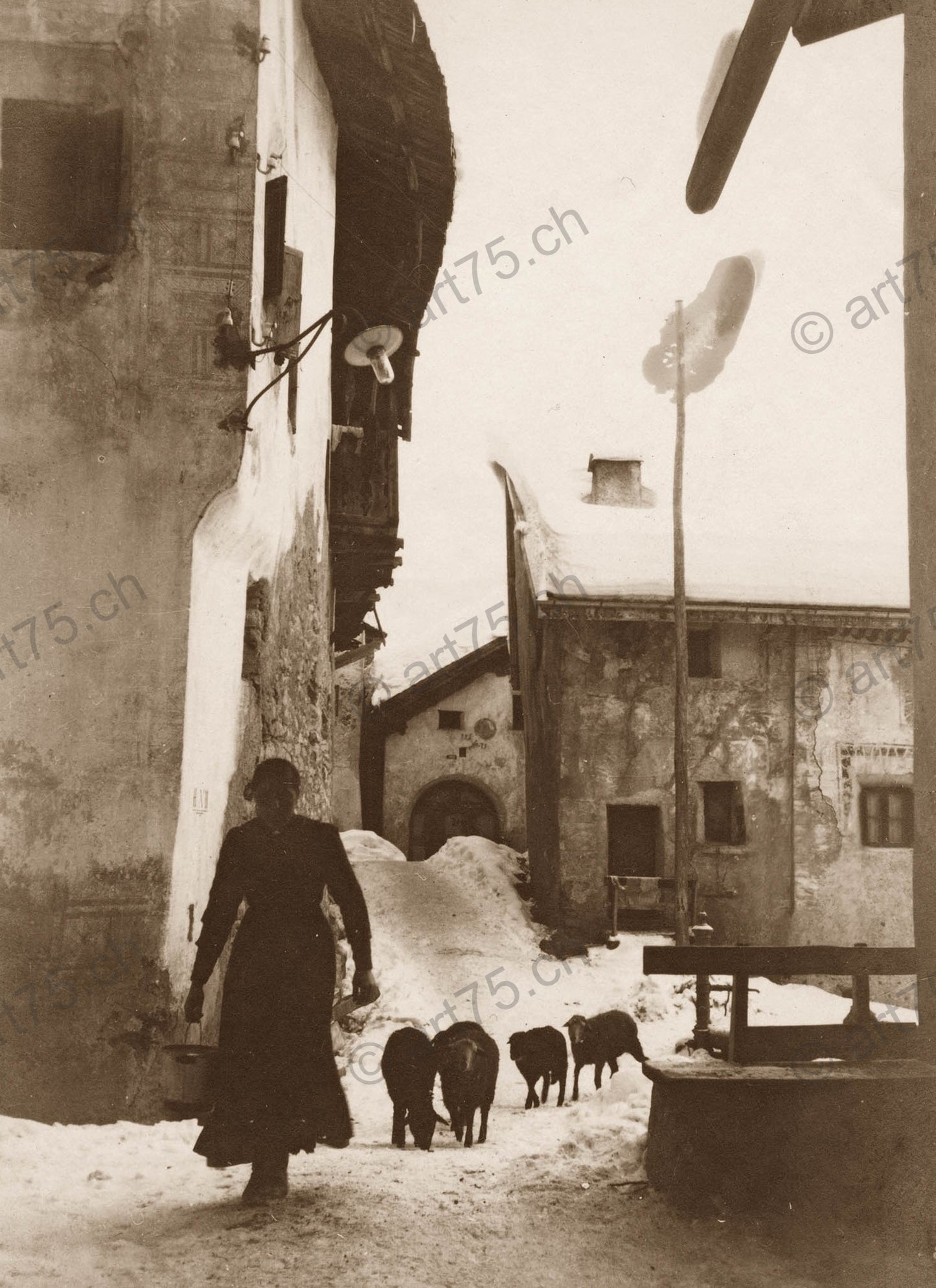 Historische Winteraufnahme aus Ardez im Engadin mit Bäuerin, Schafherde und Engadinerhäusern, um 1920.