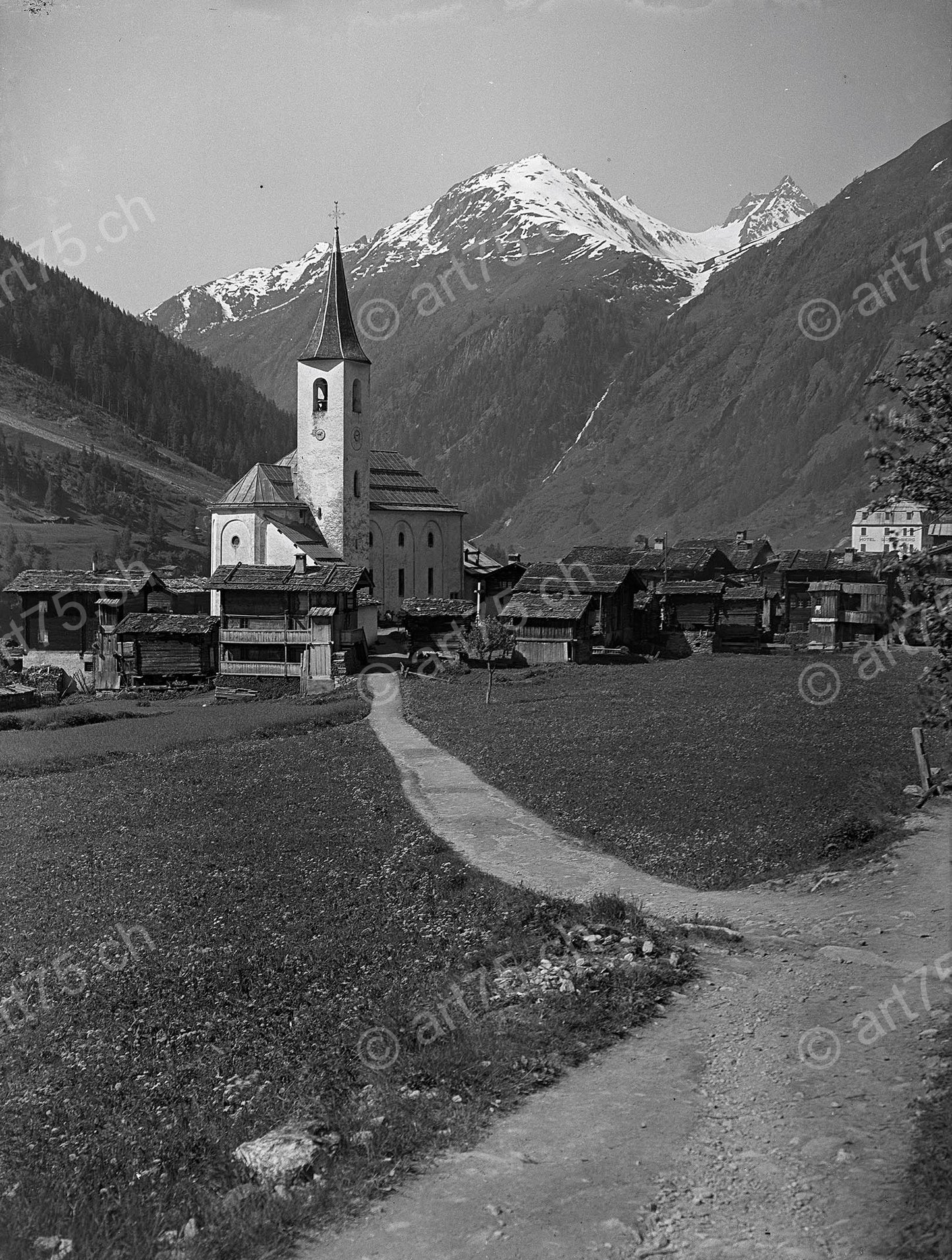 Historische Aufnahme von Kippel im Lötschental mit Pfarrkirche, traditionellen Holzhäusern und Alpengipfeln im Hintergrund, um 1930.
