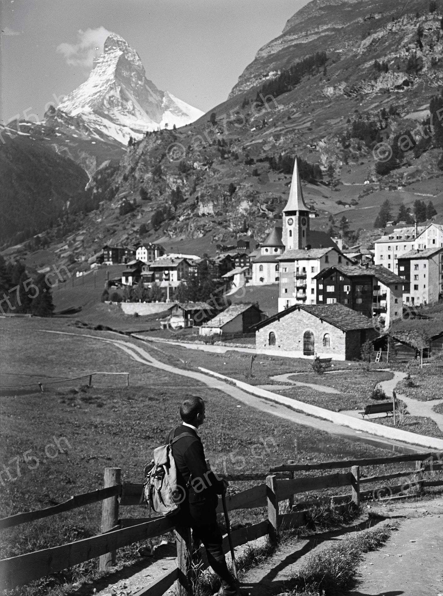 Historische Sommeraufnahme von Zermatt mit Matterhorn, Dorfkirche und einem Wanderer mit Rucksack im Vordergrund, ca. 1930.